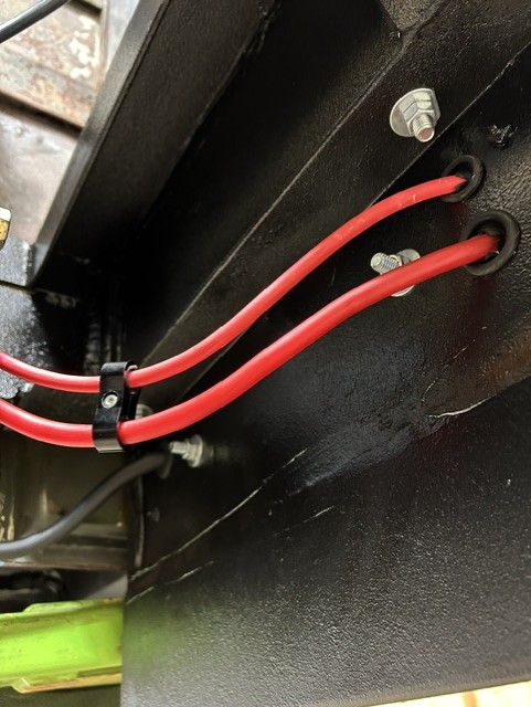 Custom red battery cables routed through a frame bracket with grommets